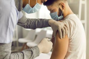 Doctor in medical face mask injecting young man with vaccine