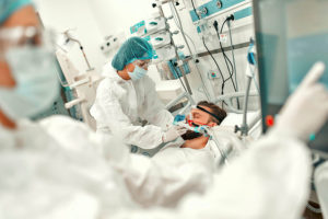 Doctors in protective suits put a ventilation mask on a man with COVID-19, who is in an intensive care unit in a modern hospital.