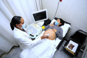 A pregnant woman undergoing an ultrasound scan and wearing a face mask