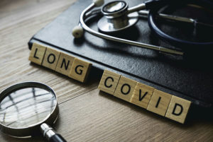 Magnifying glass, notebook, stethoscope and wooden blocks with the words Long COVID.