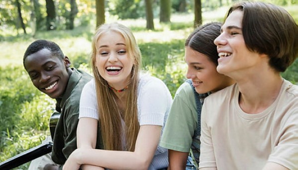 Cheerful teen friends sitting near african american boy with acoustic guitar in park